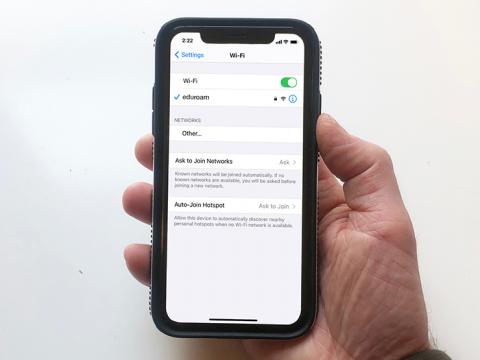 A hand holding an iPhone displaying the WiFi setting screen which shows it connected to the eduroam network.